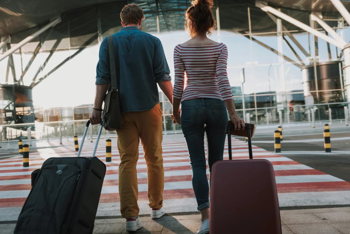 Couple walking with their wheeled suitcases through an airport terminal towards their international flight