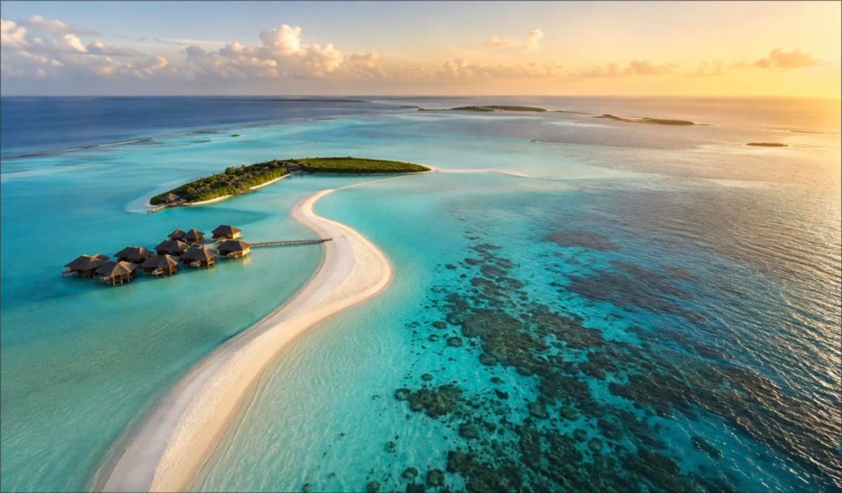 Aerial view of a Maldives atoll at golden hour with turquoise lagoons, a curving white sandbank and overwater villas