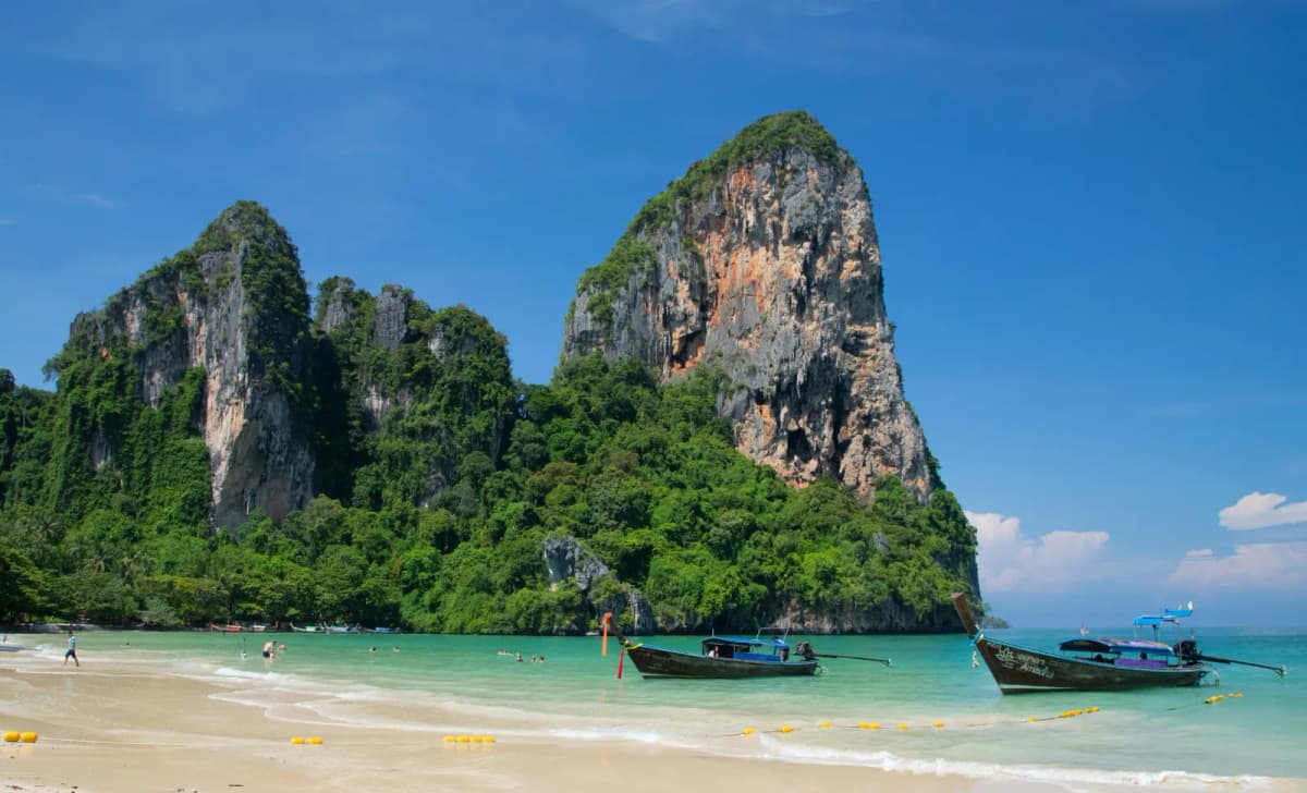 Longtail boats moored on Railay Beach beneath a huge limestone rock formation in Krabi
