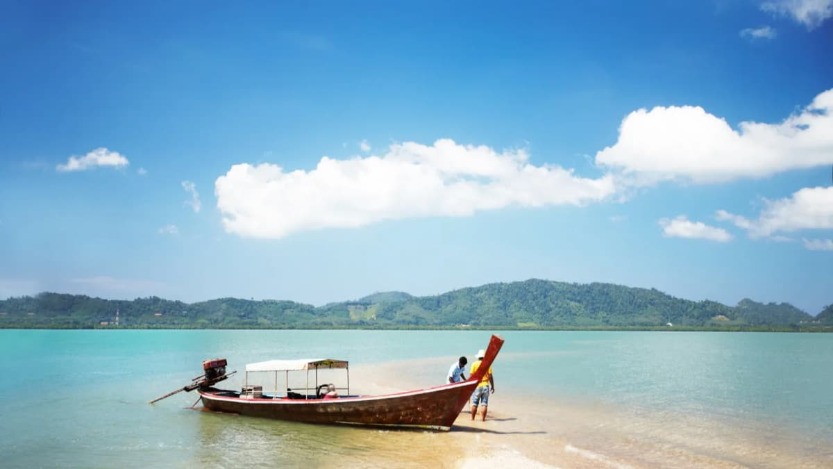 Longtail boat resting in shallow turquoise water off a quiet beach in southern Thailand