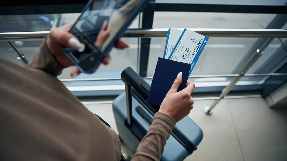 Traveller holding a passport, boarding passes and phone beside a suitcase in an airport departure area