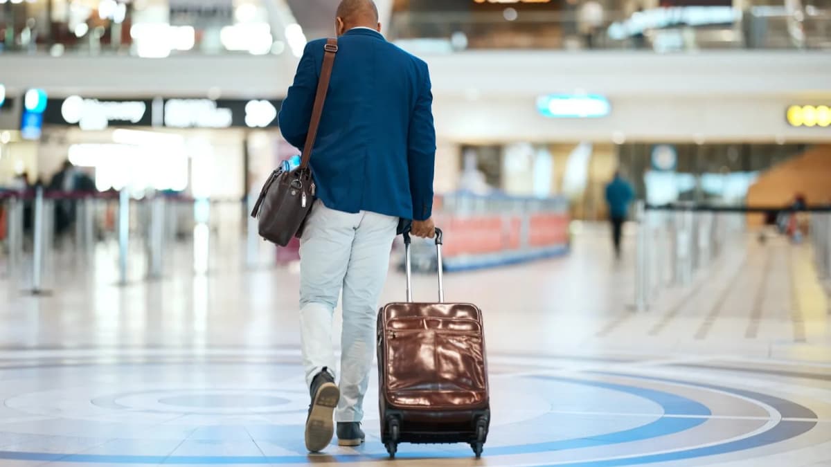 Traveller pulling a rolling suitcase through a busy airport terminal after landing