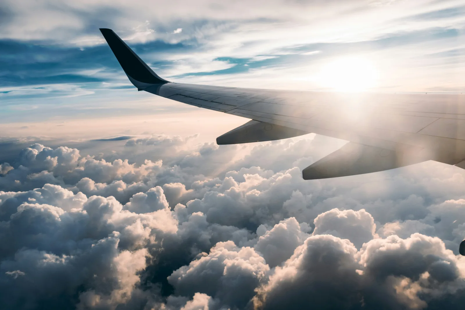 Aircraft wing above a sea of white clouds seen from a passenger window