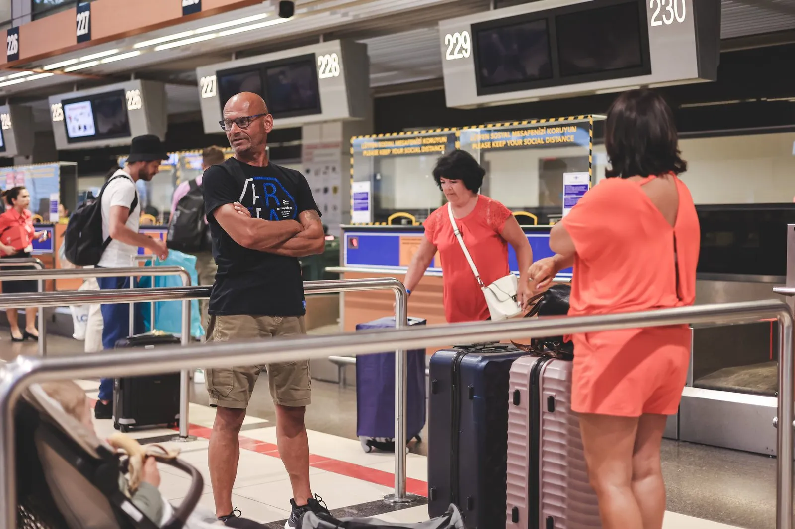 Passengers with suitcases and a stroller waiting in line at airline check-in counters