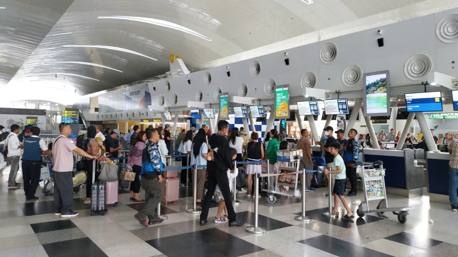 Travellers queueing at rows of airline check in counters in a busy airport hall