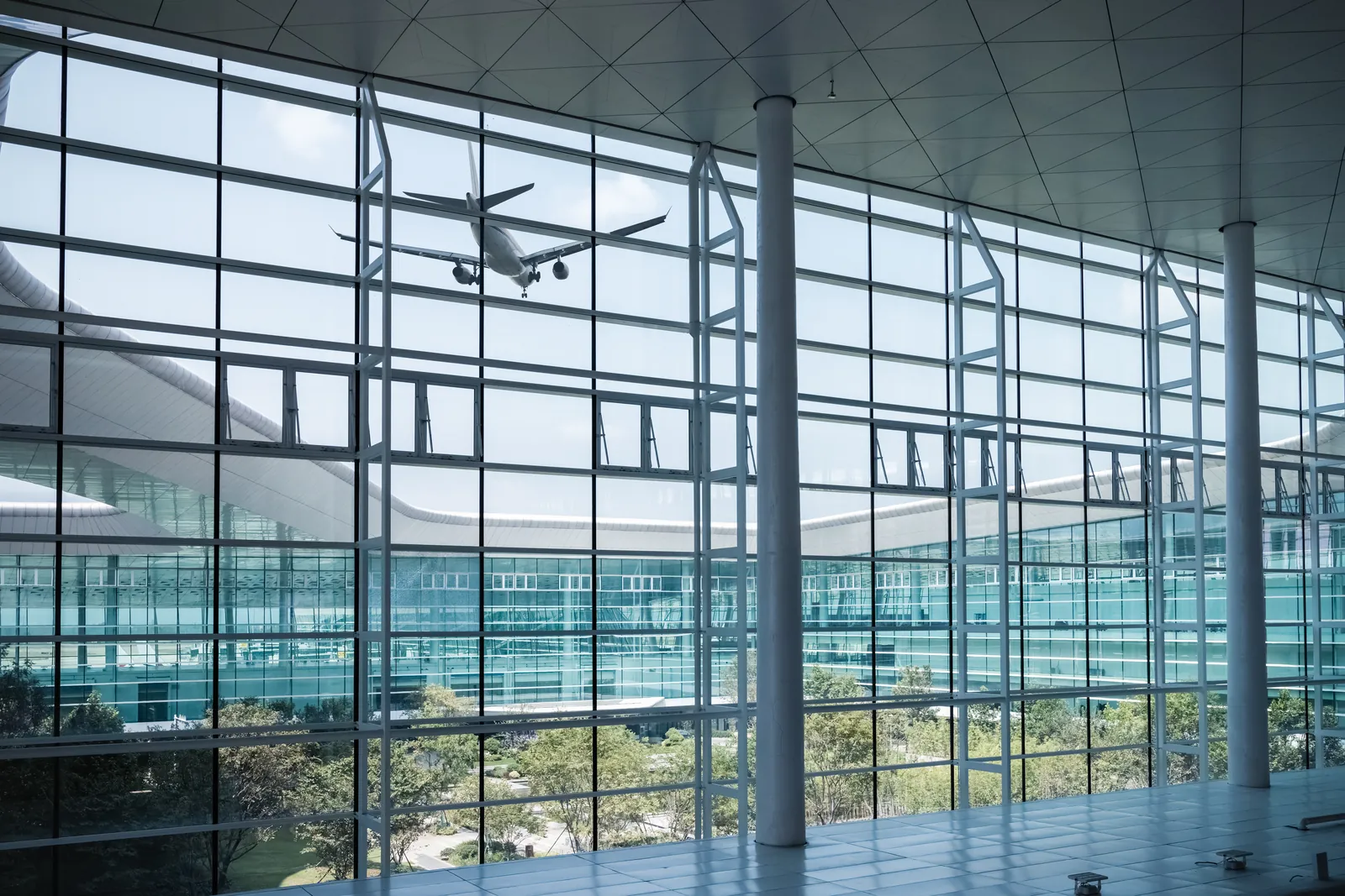 Passenger jet taking off seen through the tall glass windows of an airport terminal
