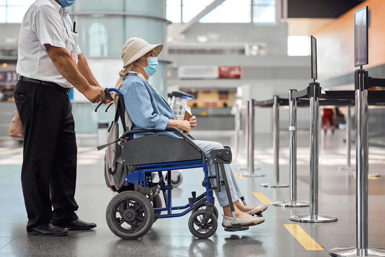 Airport staff member pushing an older traveller in a wheelchair through the check-in hall