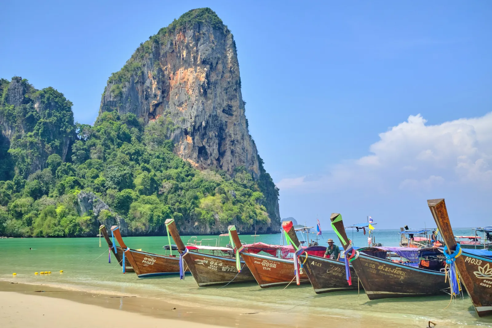 Colourful longtail boats pulled up on Ao Nang Beach below a limestone peak, Krabi