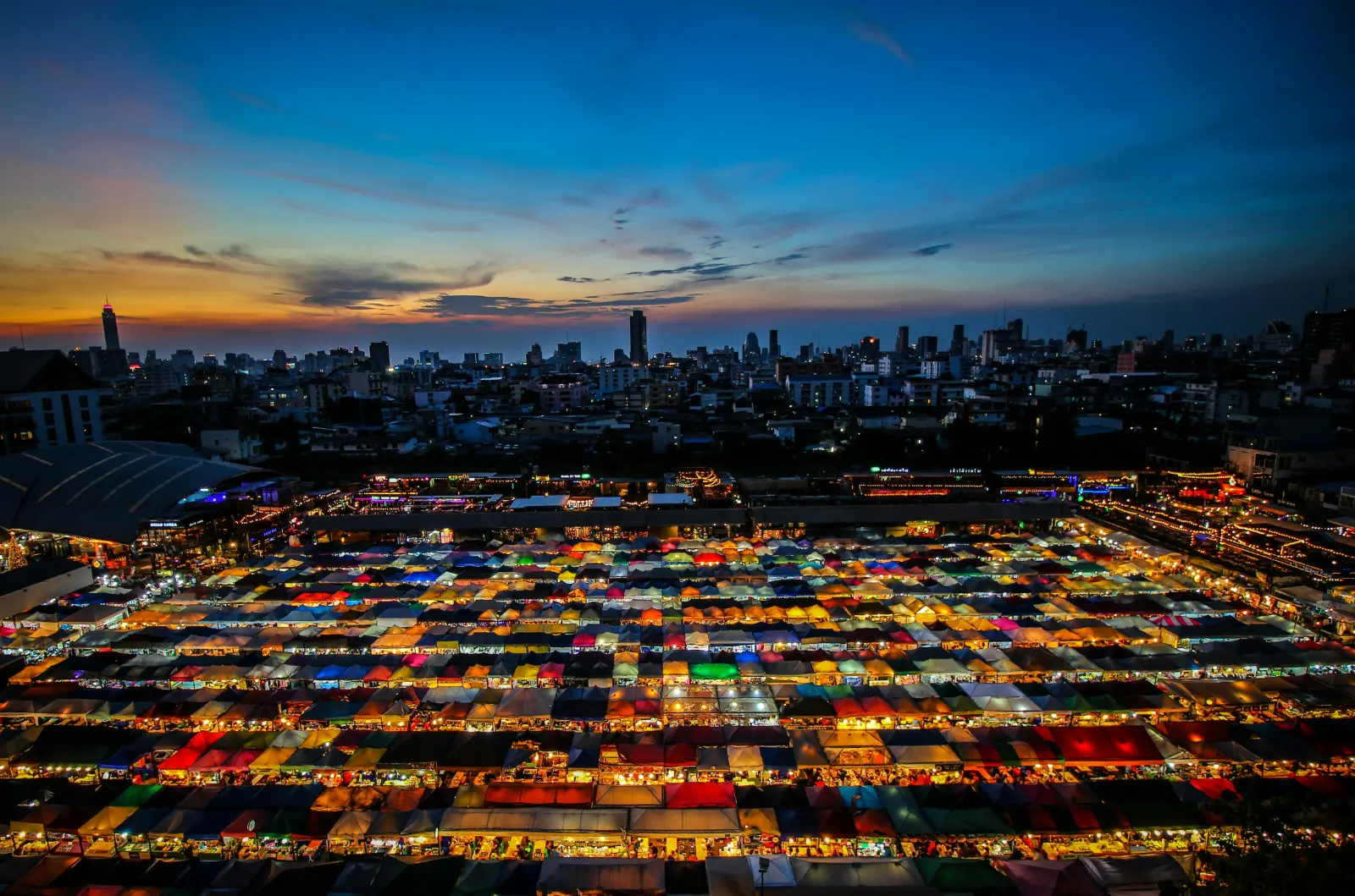 Rows of colourful stall canopies at a Bangkok night market seen from above at sunset