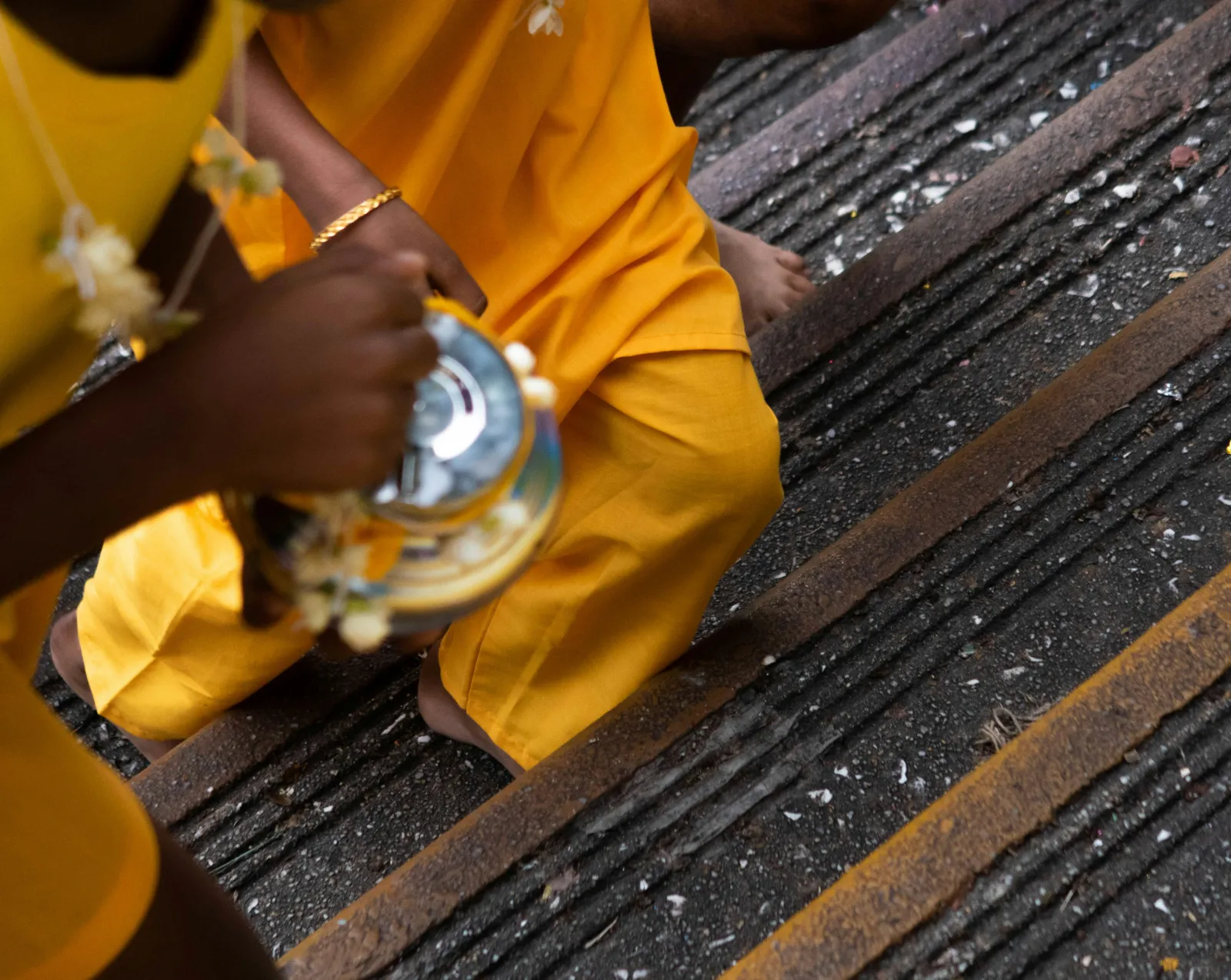 Devotee in saffron clothing carrying an offering pot up the Batu Caves staircase