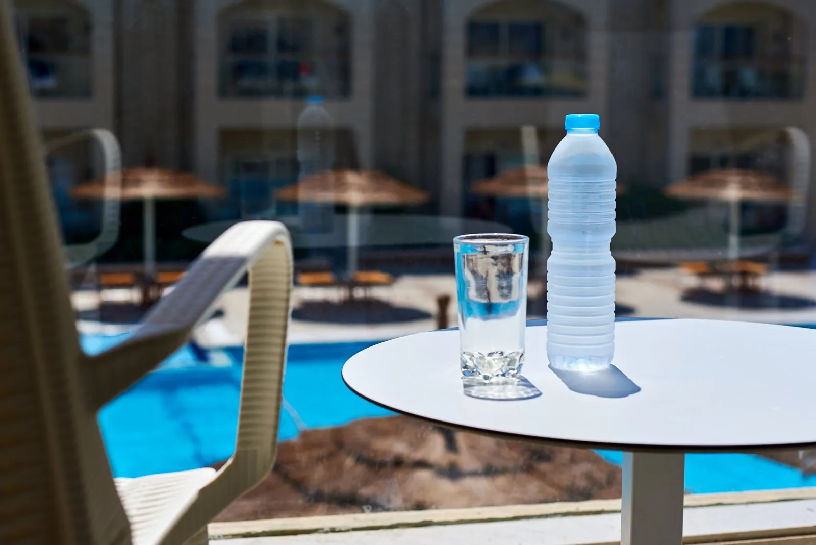 Sealed bottle of drinking water and a glass on a poolside table at a tropical hotel