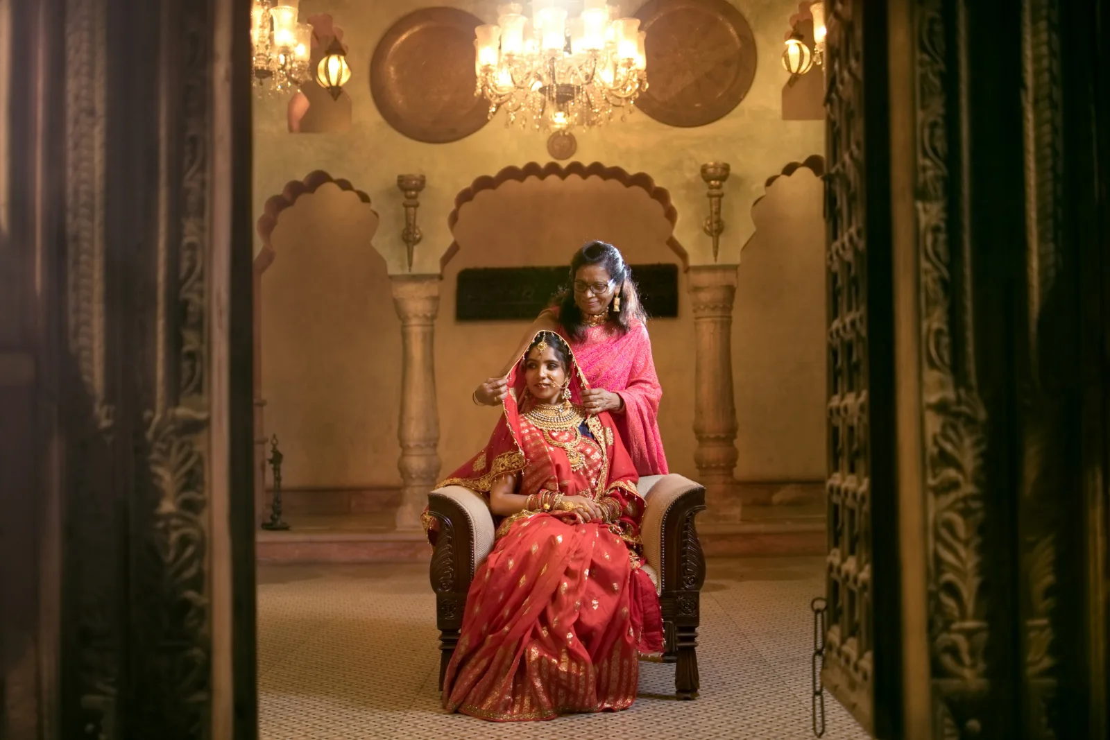 South Asian bride in a red traditional wedding outfit seated in an ornate hall
