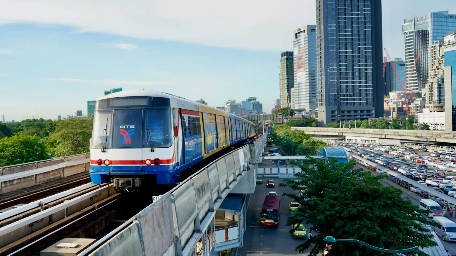 BTS Skytrain running on an elevated track through central Bangkok traffic and towers