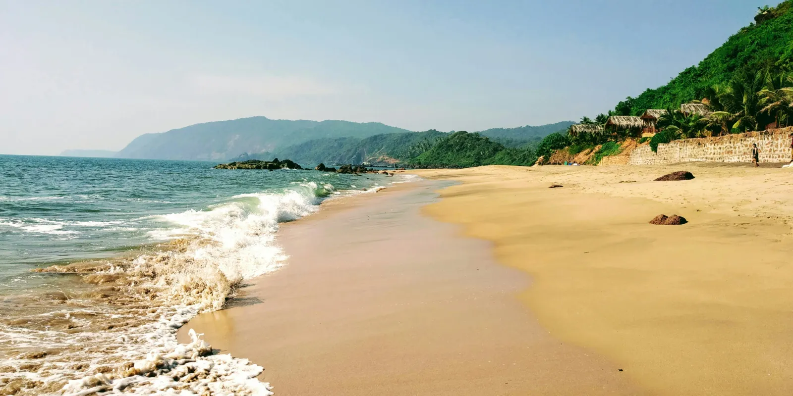 Golden sand and gentle surf below green wooded hills at Cola Beach in South Goa