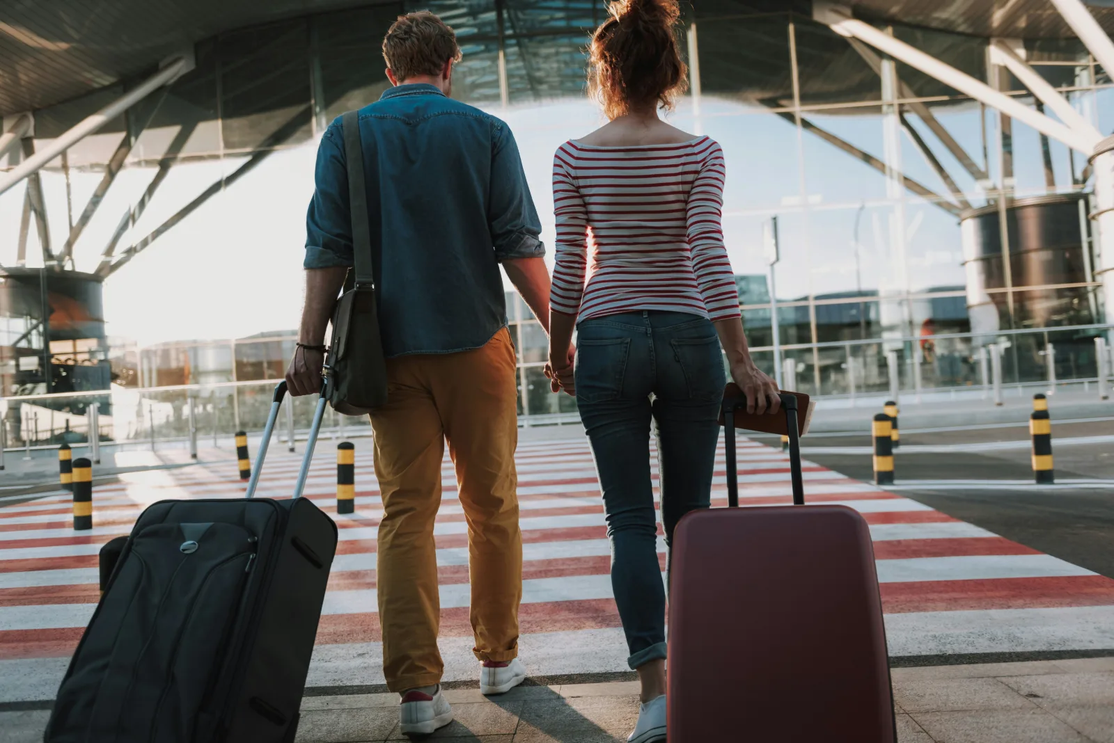Couple walking hand in hand with suitcases through an airport departure area