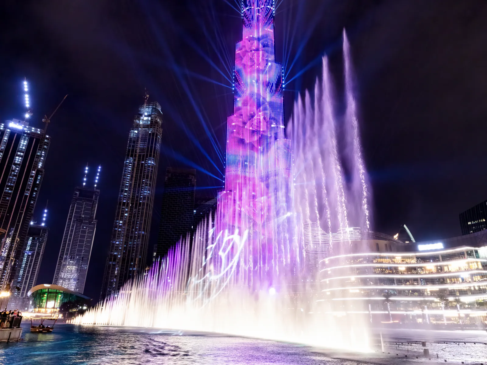 Dubai Fountain jets lit purple in front of the illuminated Burj Khalifa at night