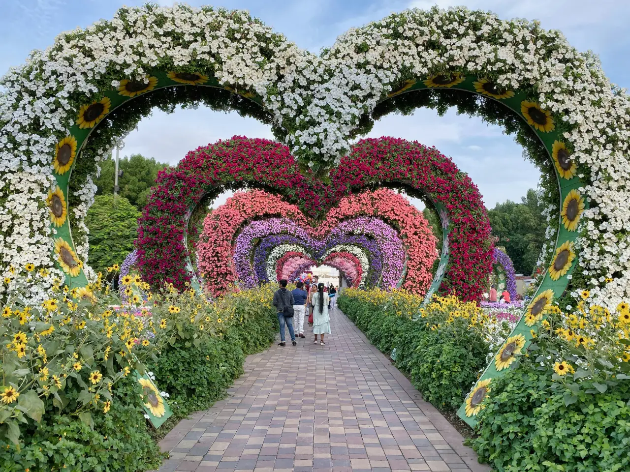 Visitors walking under pink and red floral heart arches at Dubai Miracle Garden