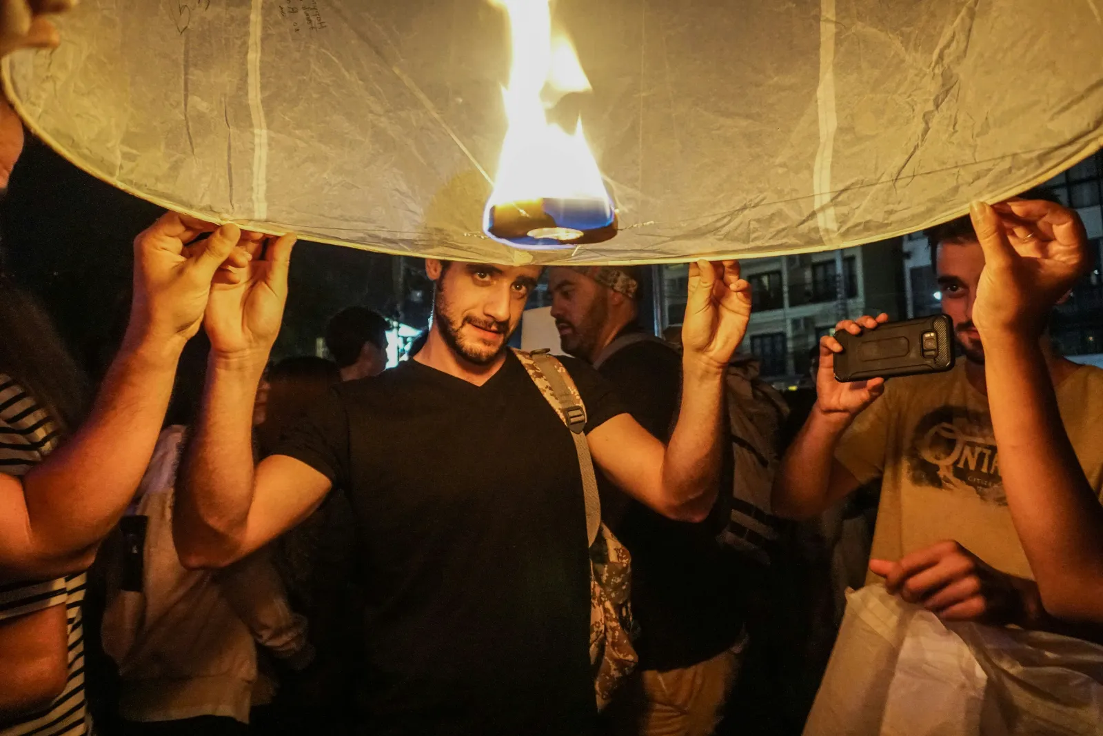 Group of friends holding a lit paper sky lantern together just before releasing it