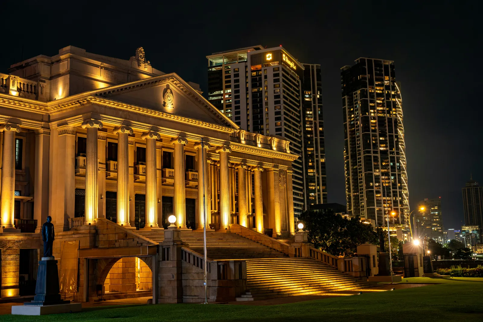 Floodlit colonial era building and modern towers beside Galle Face in Colombo at night