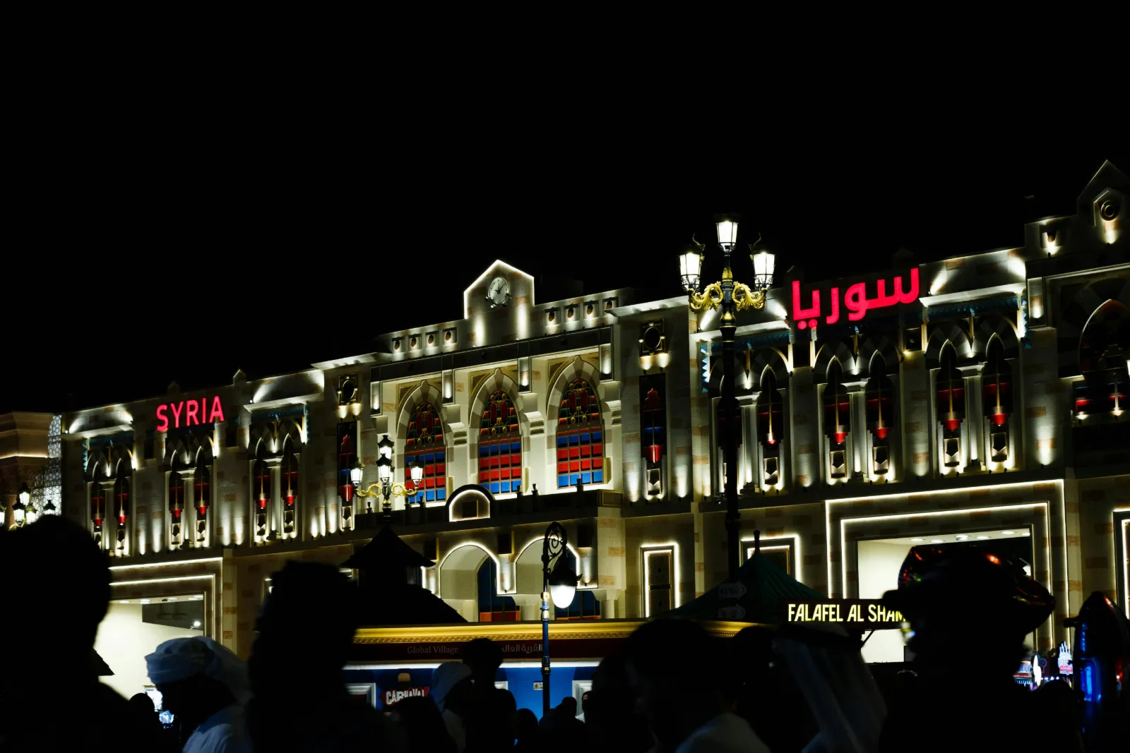 Illuminated country pavilion facade at Global Village Dubai with evening crowds outside