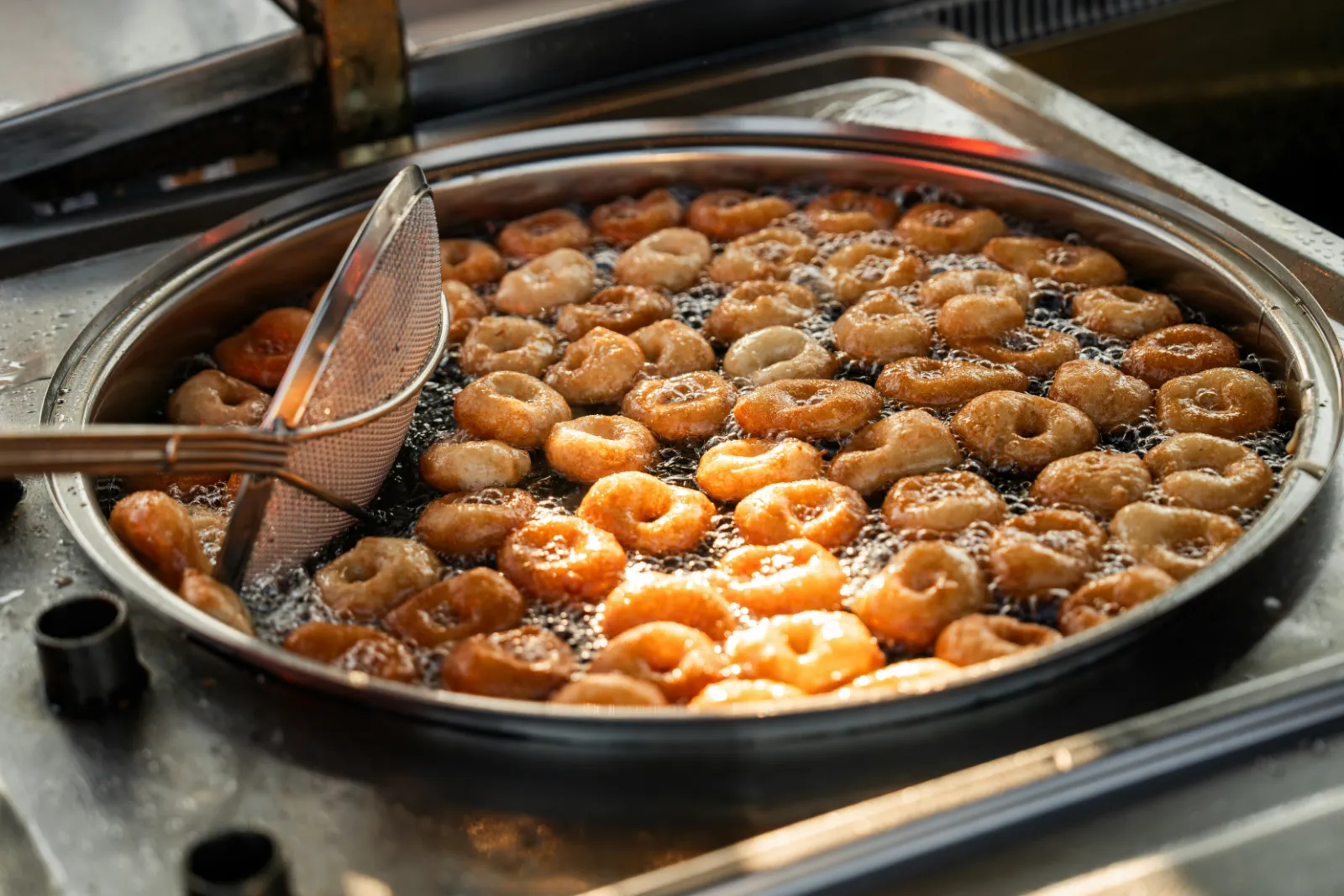 Golden fried dough balls cooking in a large pan, a sweet much like Emirati luqaimat