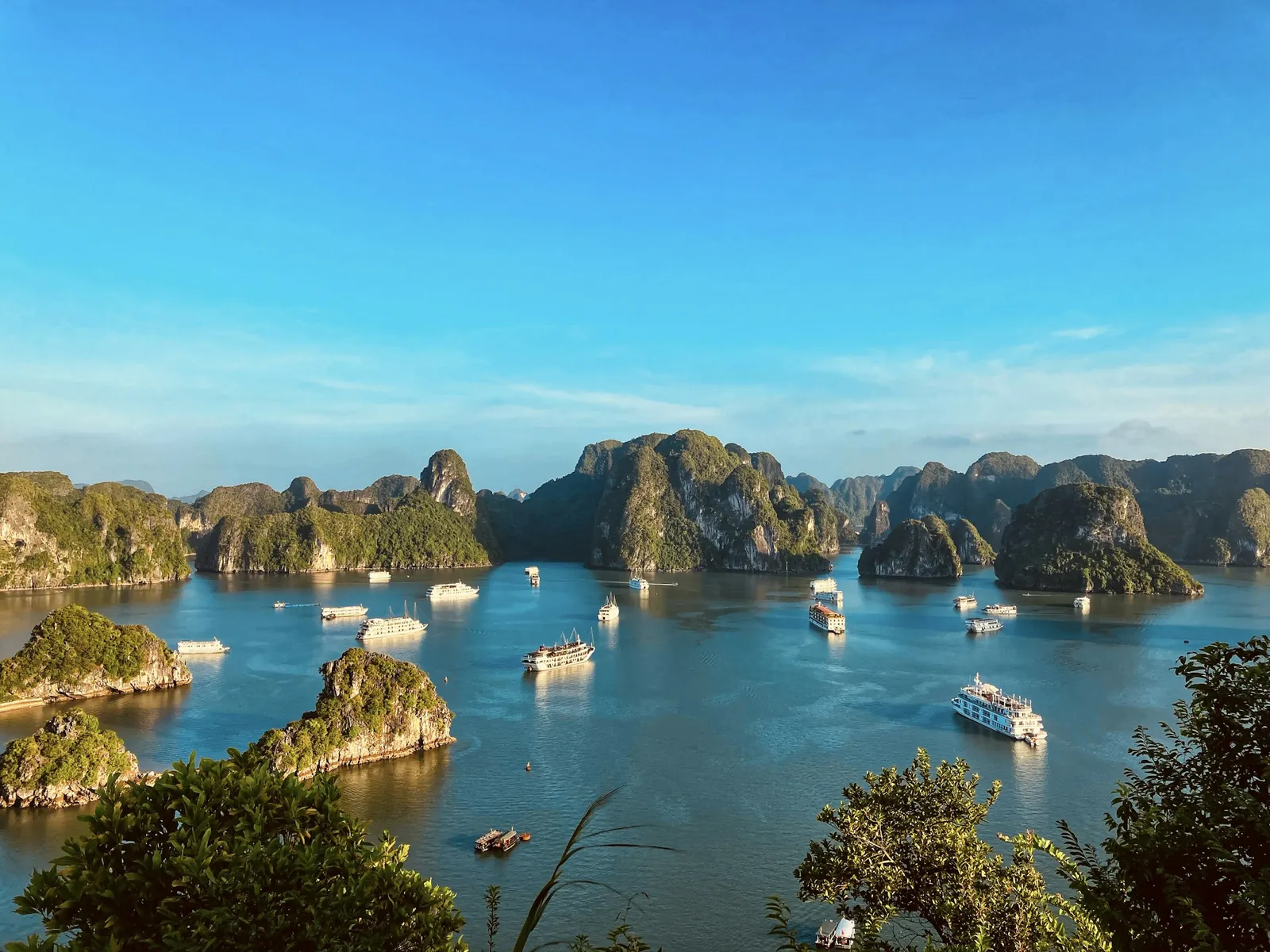 Cruise boats sailing between limestone islands in Ha Long Bay under a blue sky