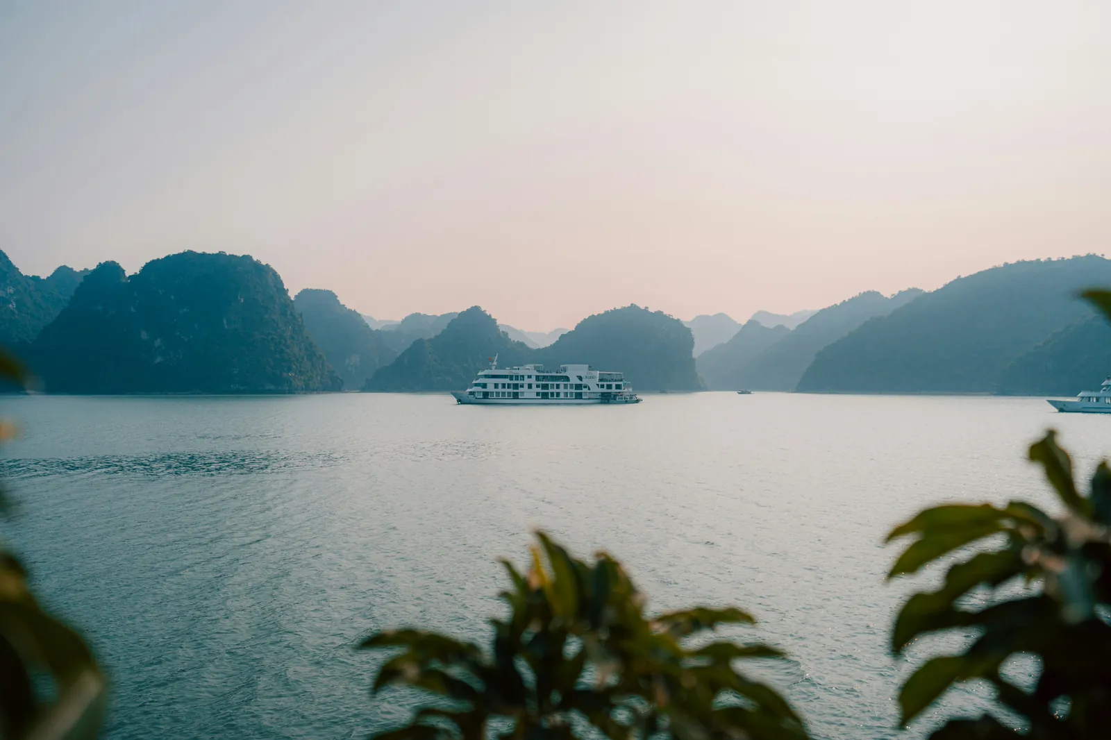 Cruise boat sailing between limestone karst islands in Ha Long Bay, Vietnam, on a misty morning