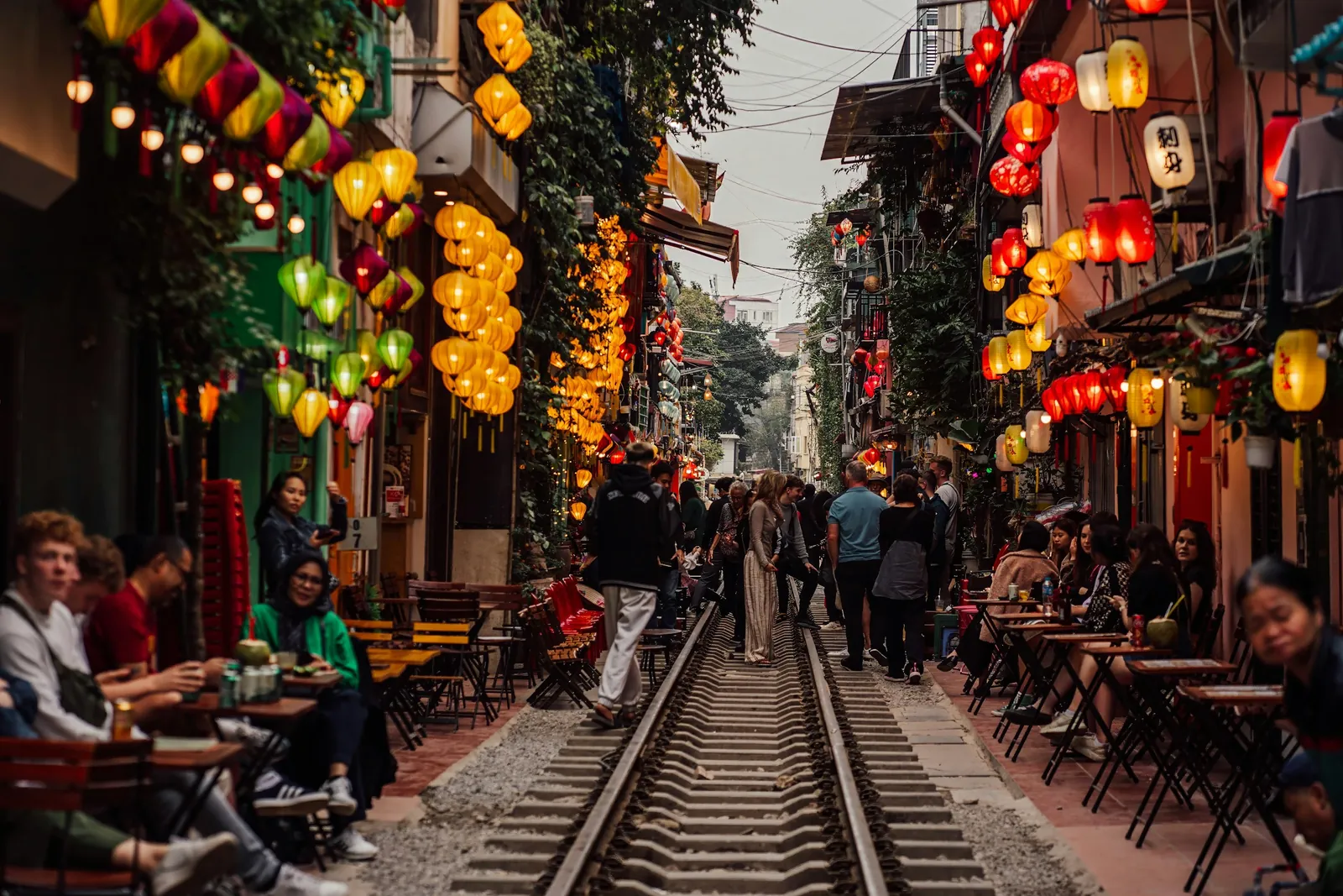 Visitors at cafe tables along the railway track on Hanoi Train Street under lanterns