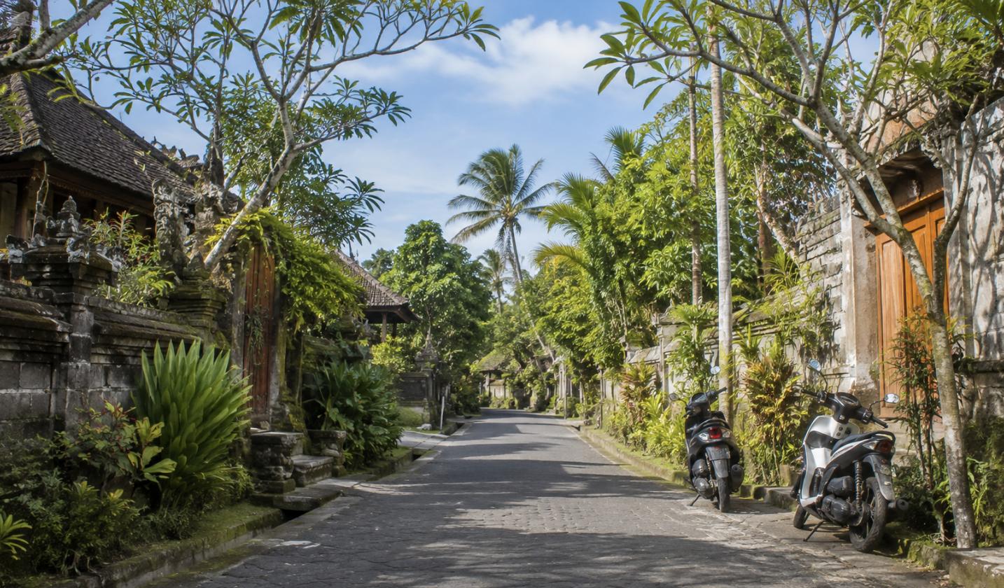 A peaceful Bali village street with parked scooters and tropical greenery
