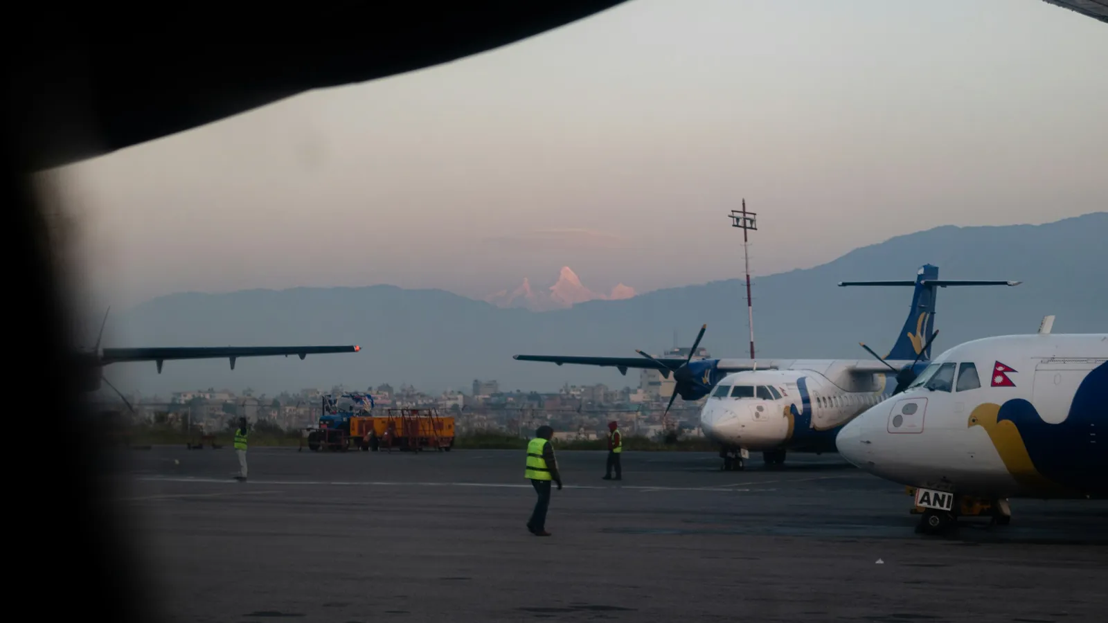 Turboprop aircraft parked on the apron at Kathmandu airport at sunrise with hills behind