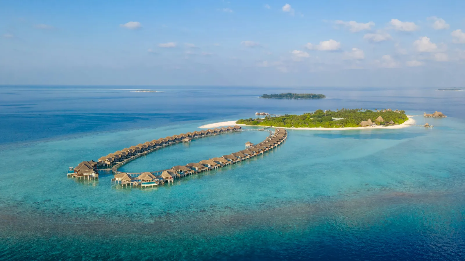Small island with overwater villas ringed by a coral reef and lagoon in the Maldives