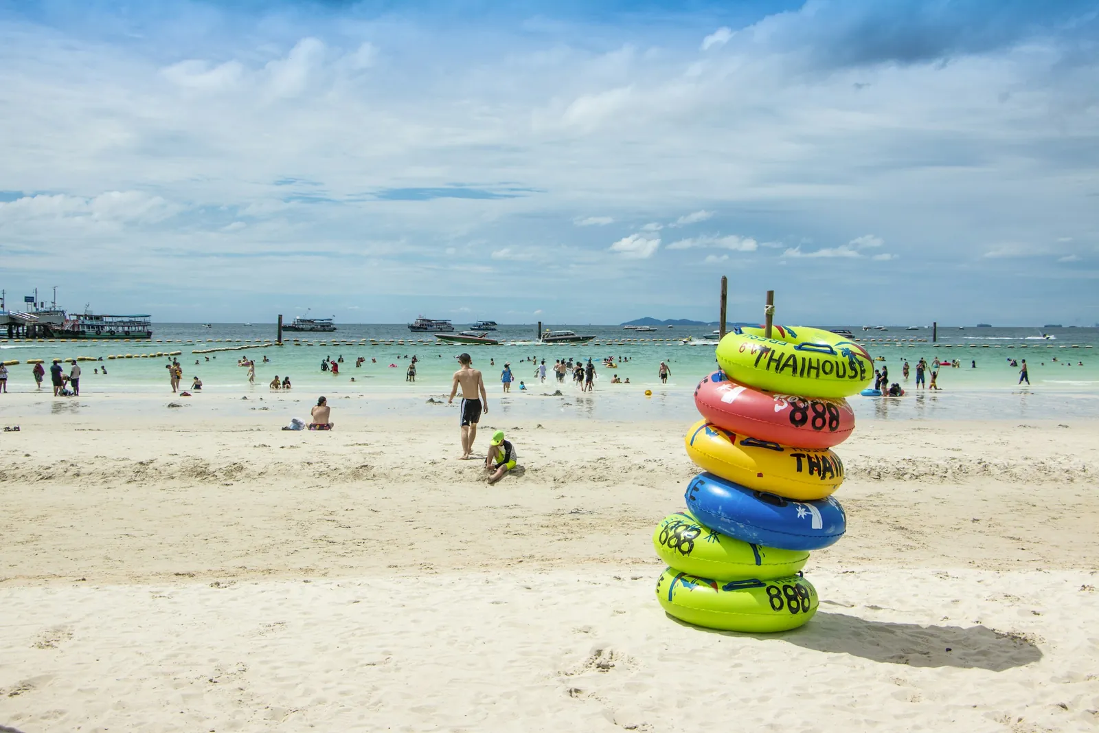 Swimmers and colourful rubber rings on a white sand beach on Koh Larn near Pattaya