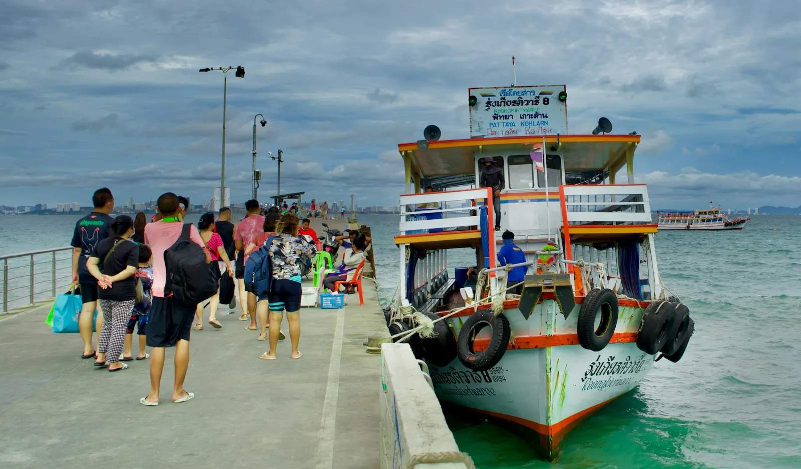 Passengers boarding a Koh Larn ferry at the pier on a cloudy day near Pattaya
