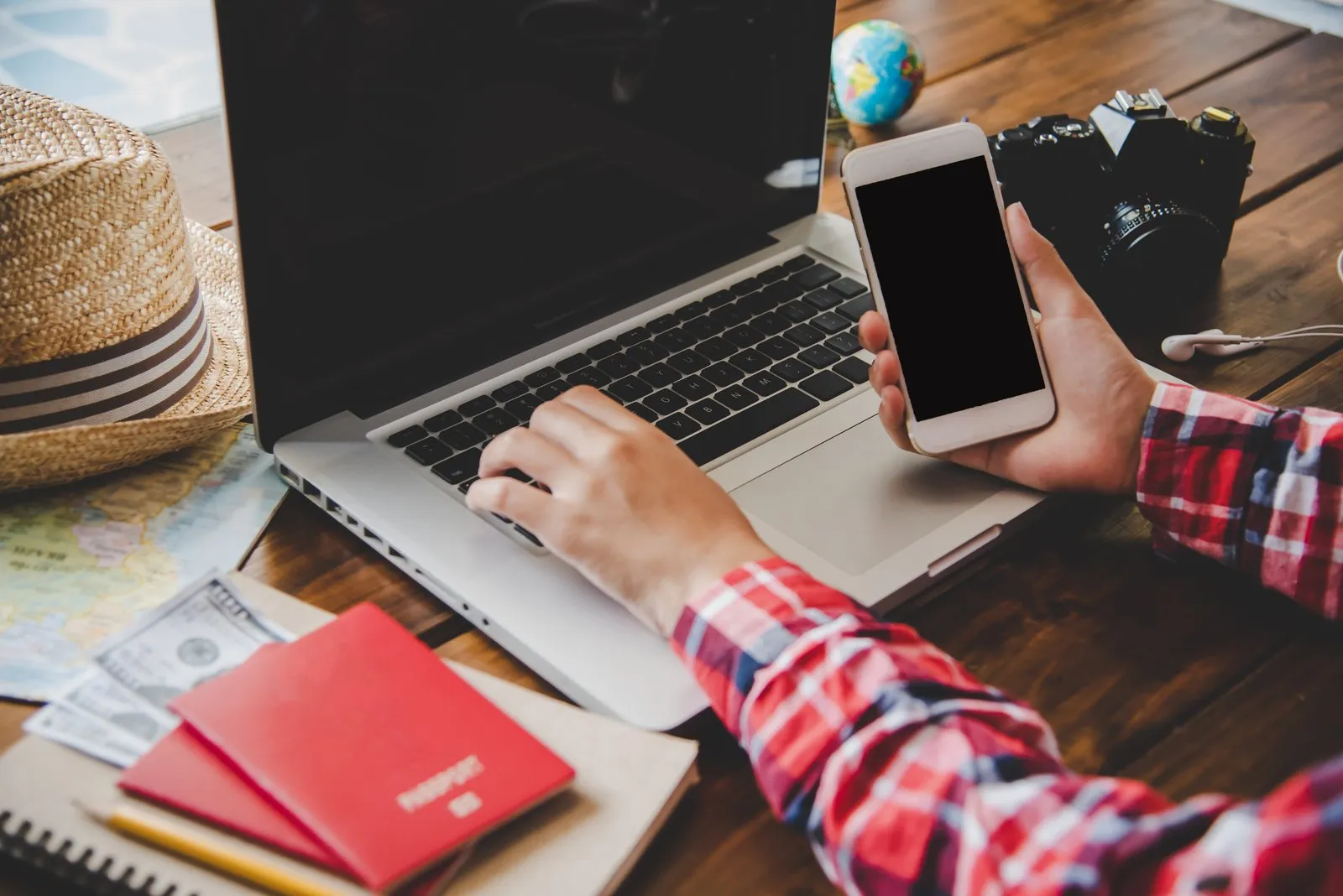 Traveller using a laptop and smartphone at a desk with passports ready for a trip
