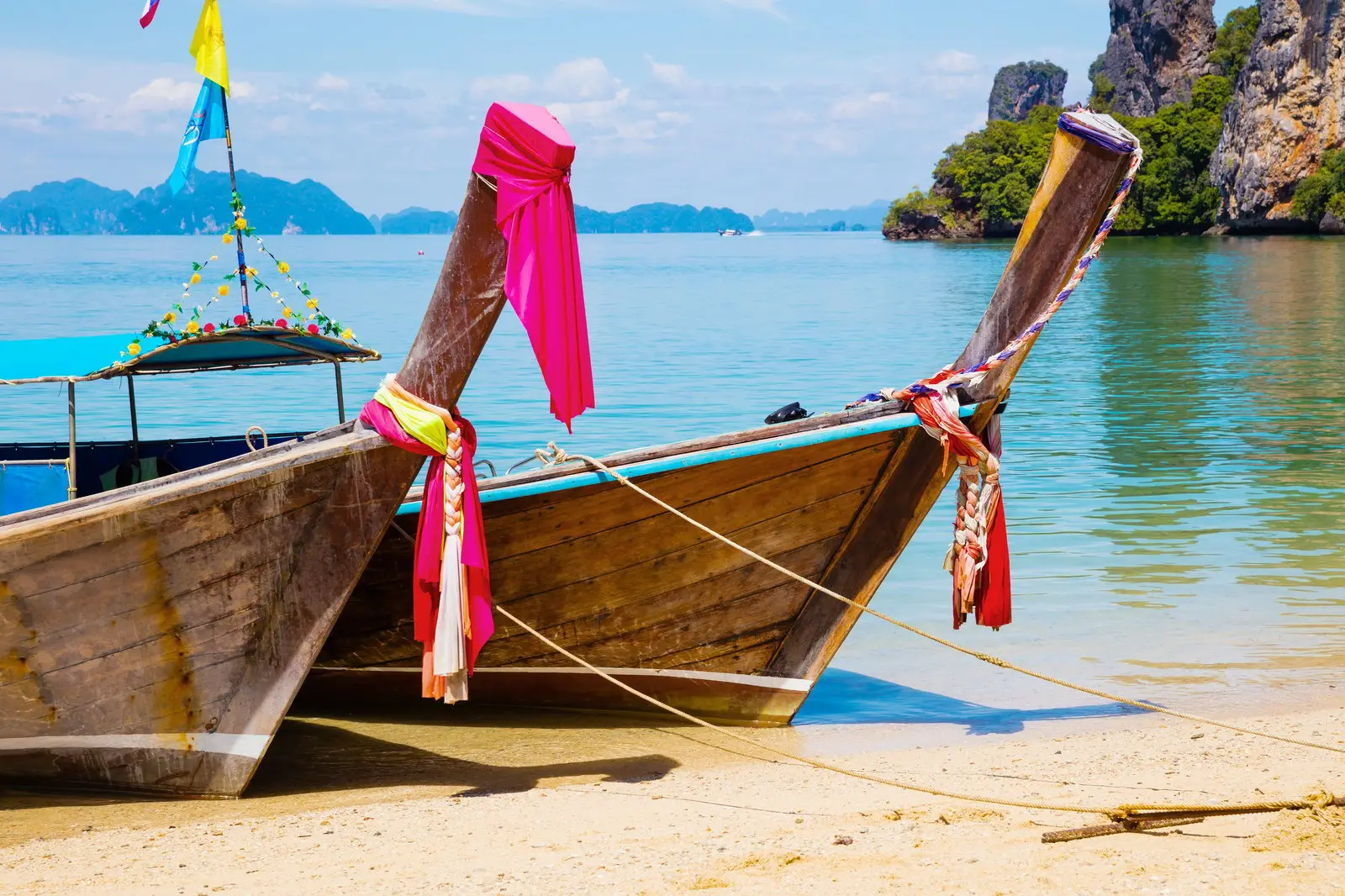 Wooden longtail boats with ribbons pulled onto a beach below limestone cliffs in Thailand