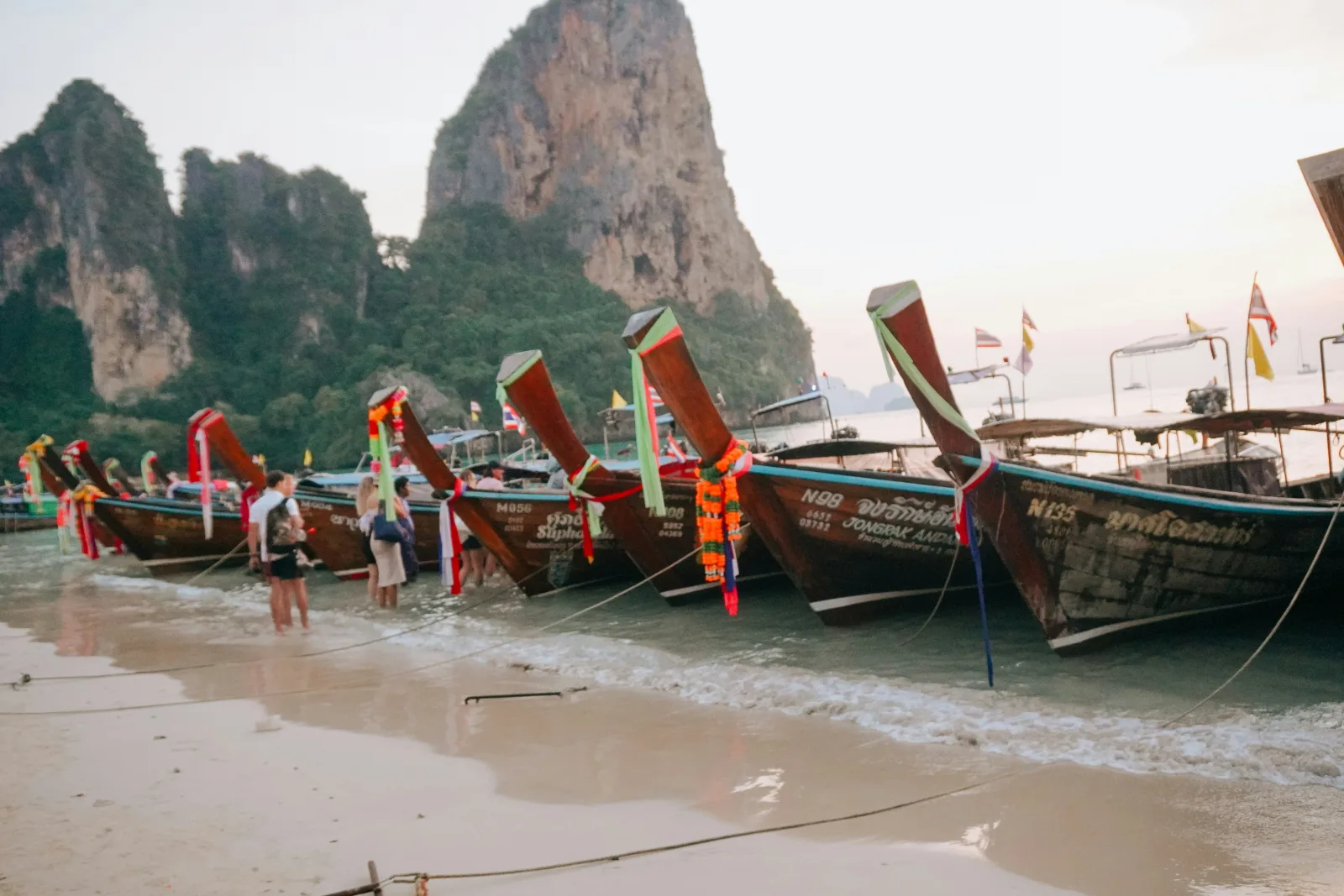 Longtail boats lined up on a Thai beach beneath tall limestone cliffs