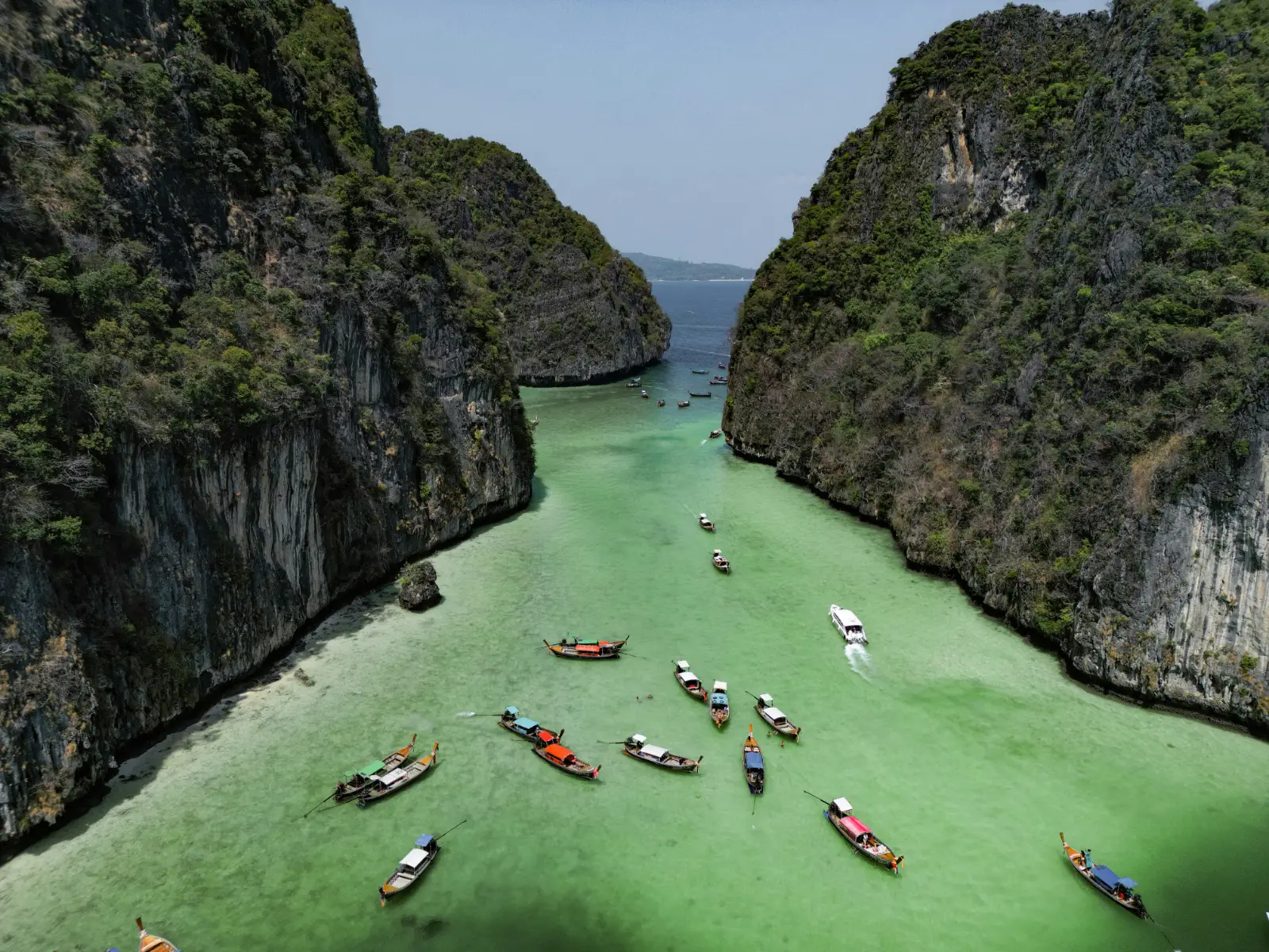 Longtail boats moored in a turquoise lagoon between limestone cliffs on a Thai island