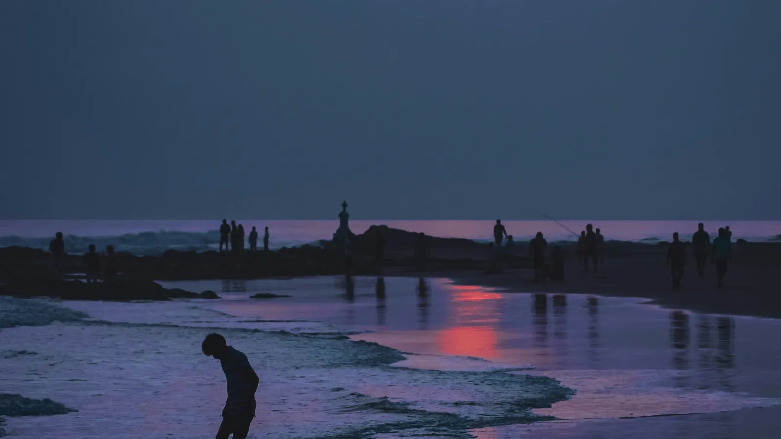 Fisherman silhouetted against the sunset sky on the wide flat sand of Morjim Beach, North Goa