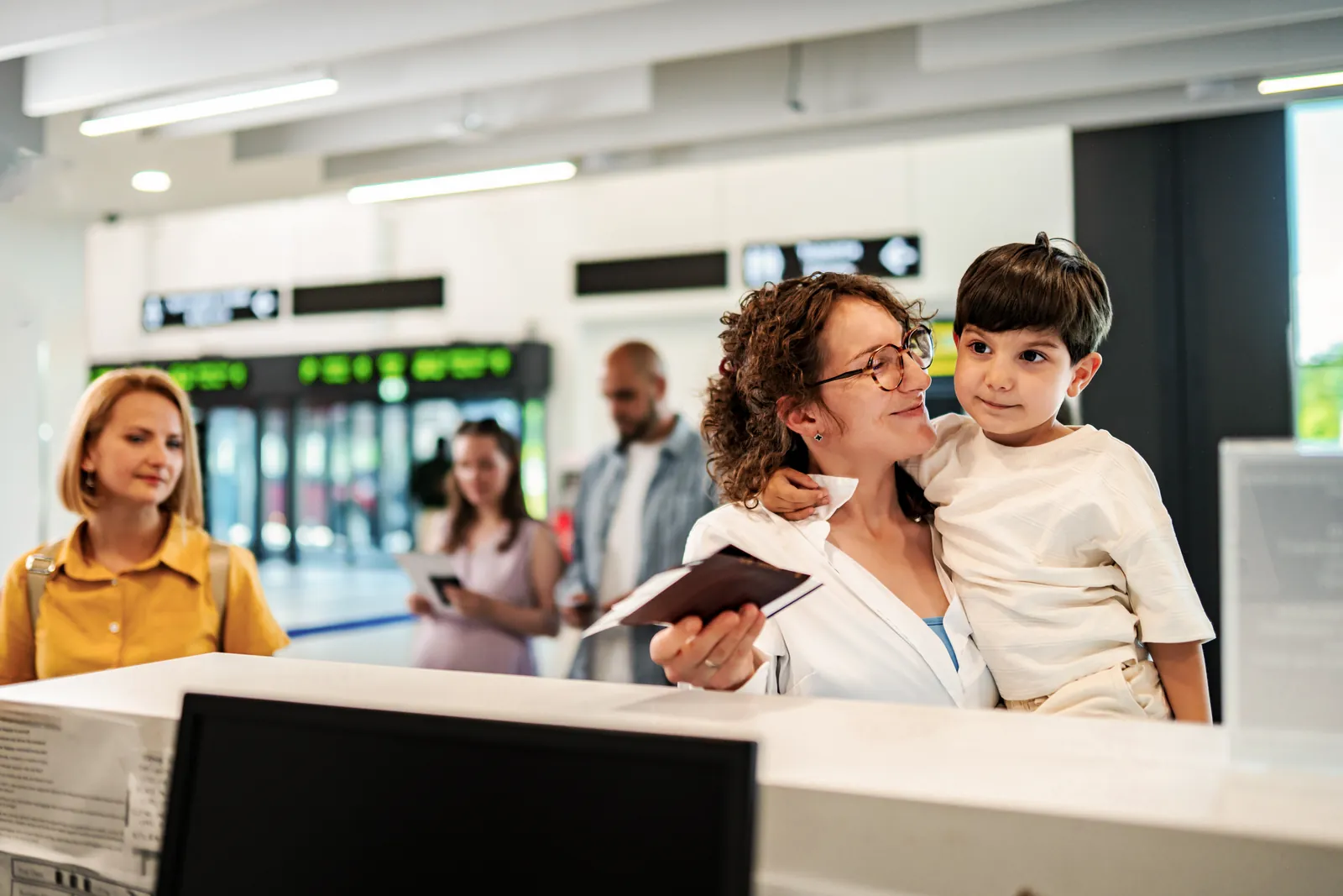 Mother holding her young son while showing travel documents at an airline check in counter