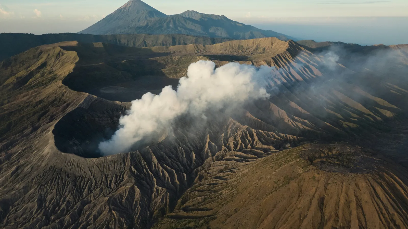 High view into the active Mount Bromo crater with white volcanic smoke rising from the vent
