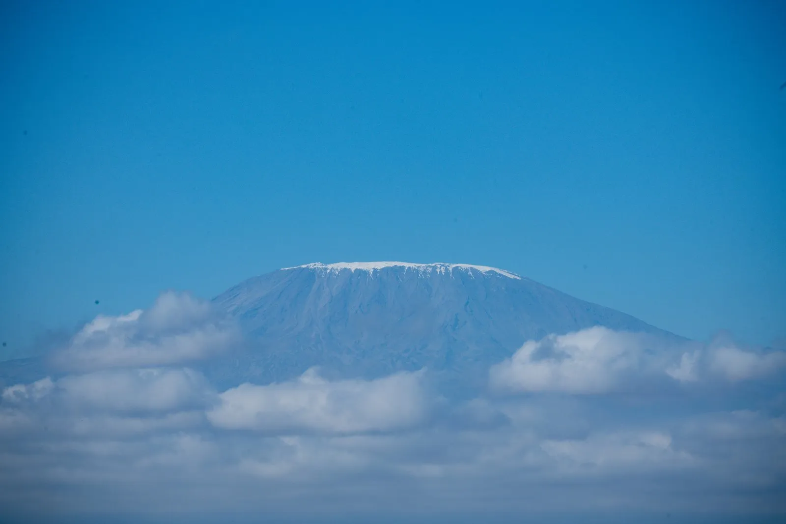 Snow capped summit of Mount Kilimanjaro rising above a band of clouds in Tanzania
