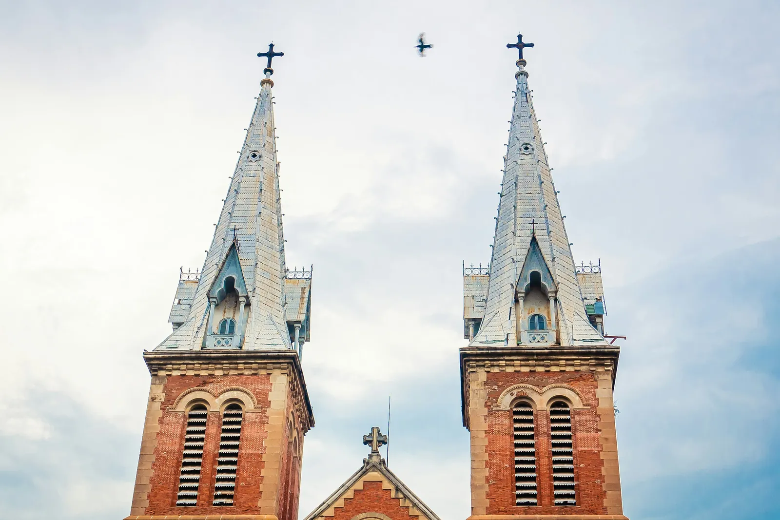 Twin red brick spires of Notre Dame Cathedral Basilica of Saigon against a blue sky