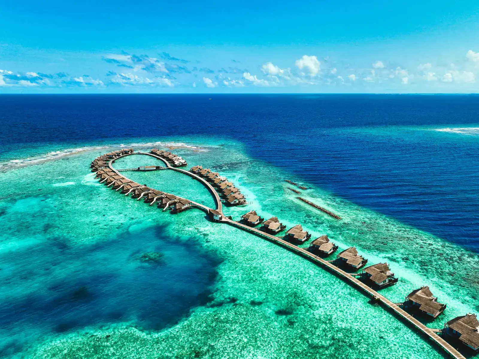 Curving rows of overwater villas at Ozen Reserve Bolifushi resort island in the Maldives