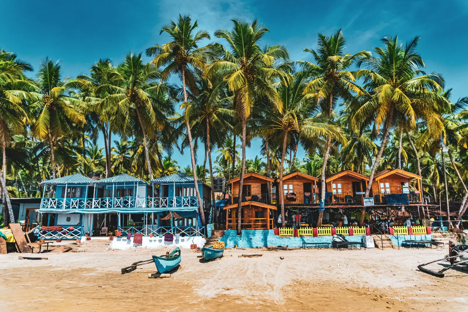 Colourful beach huts beneath tall coconut palms on Palolem Beach, South Goa