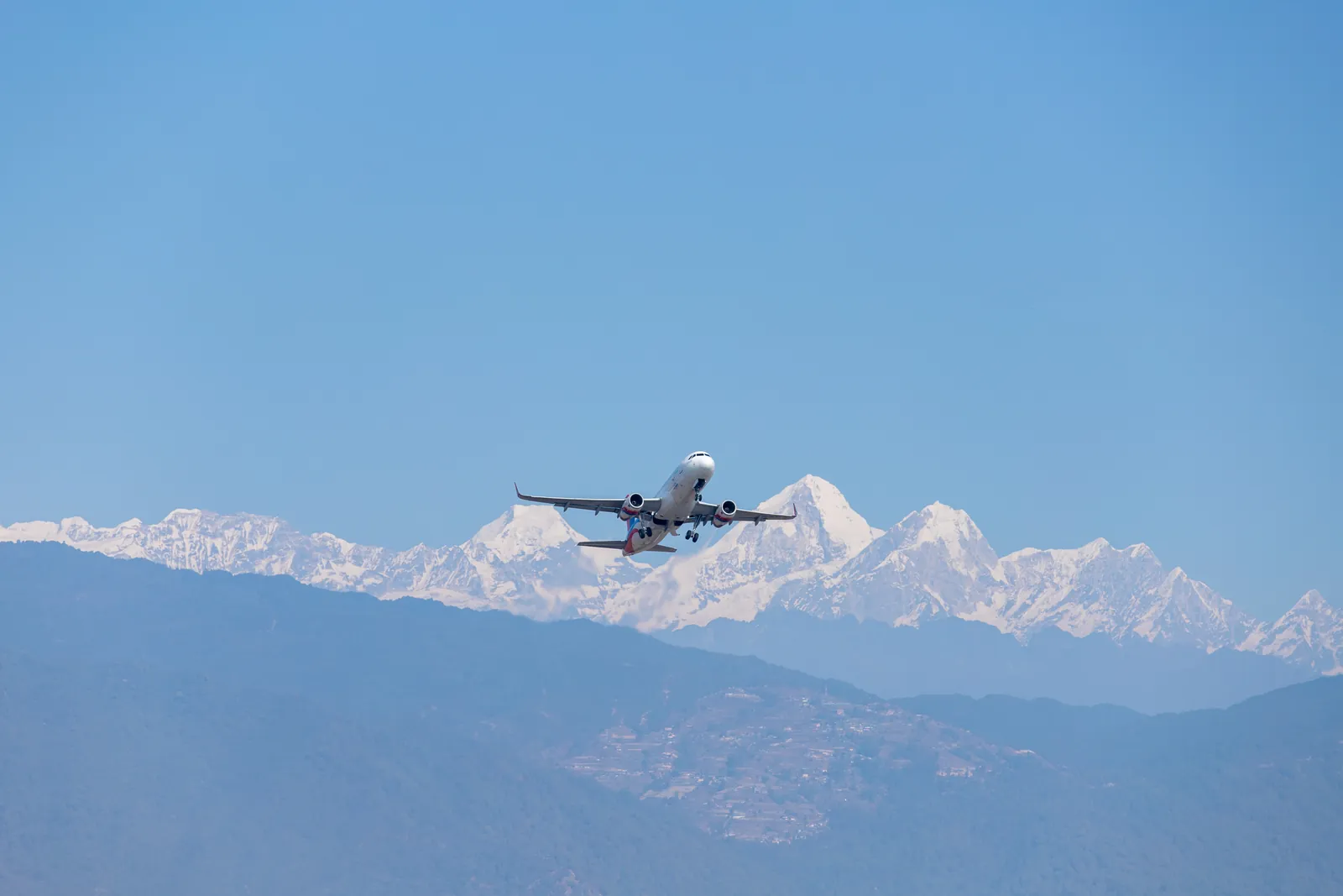 Passenger jet flying past a long snow capped mountain range on a clear blue morning