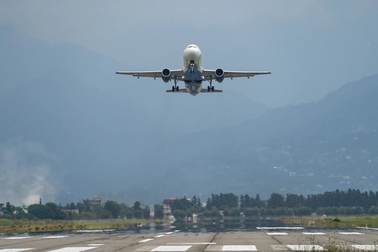 Passenger jet lifting off a runway with hazy green hills behind it