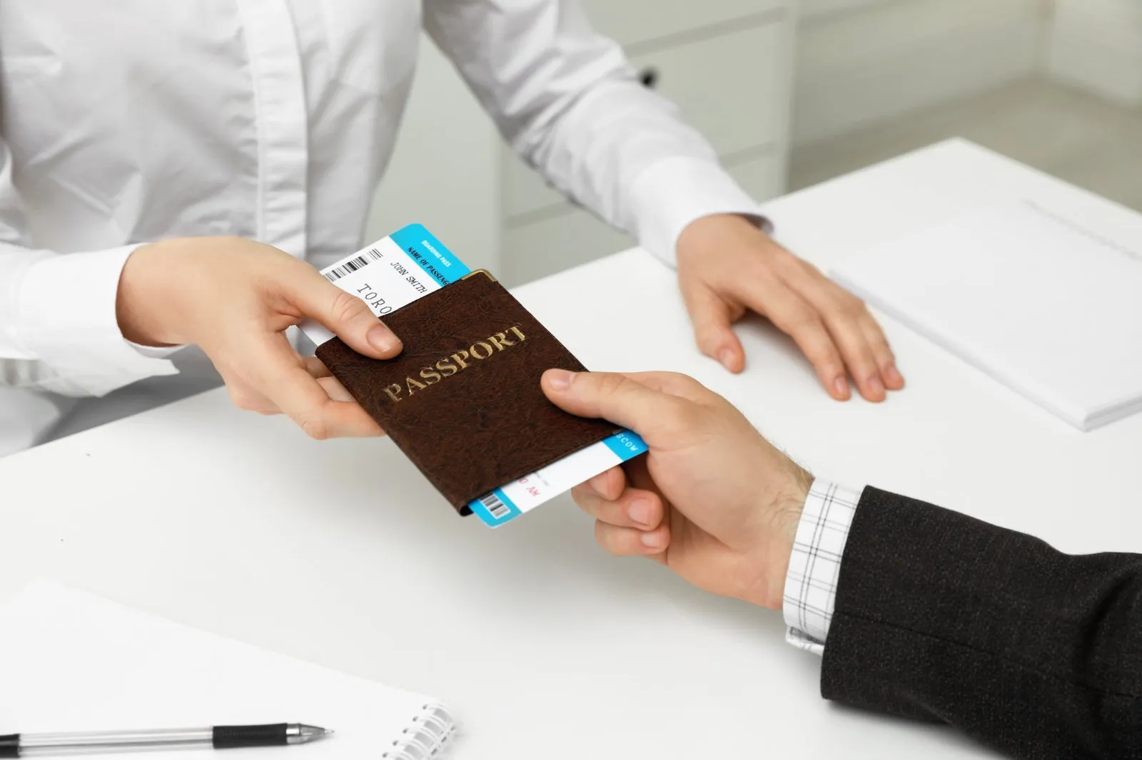 Passport with a boarding pass tucked inside being handed across a desk to an officer