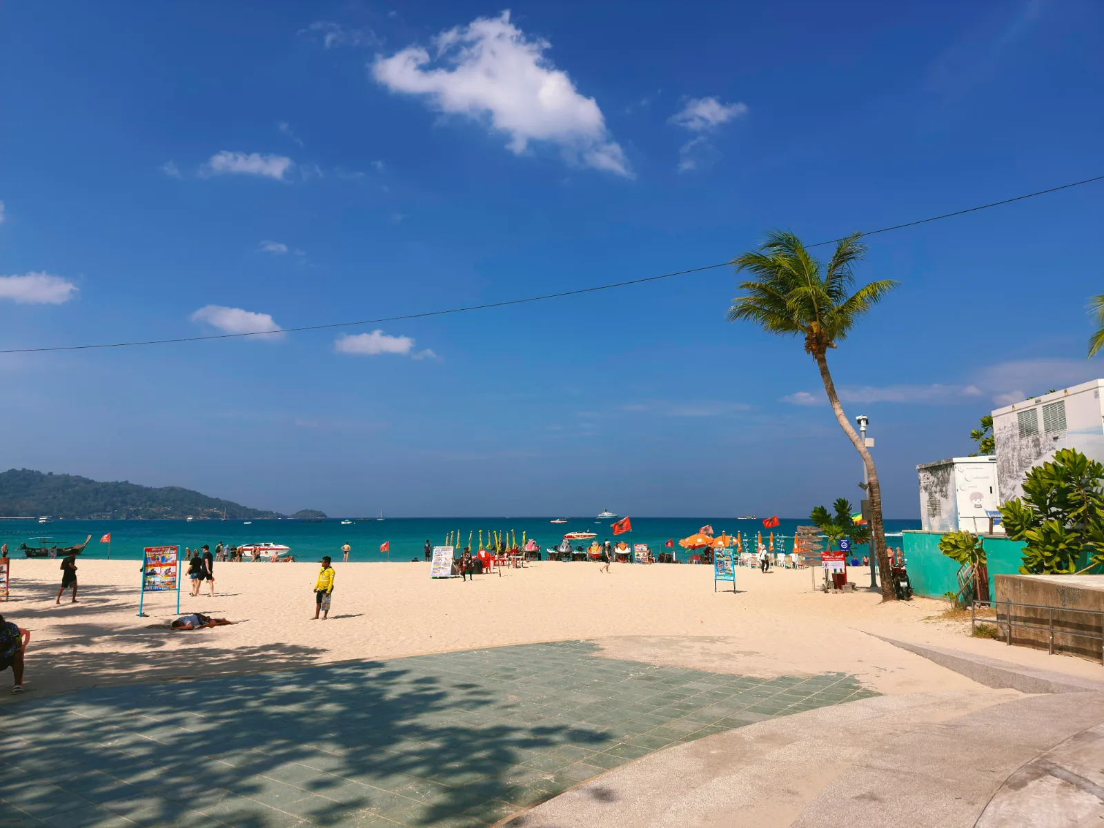 Sunny day on Patong Beach in Phuket with umbrellas, palms and blue sea