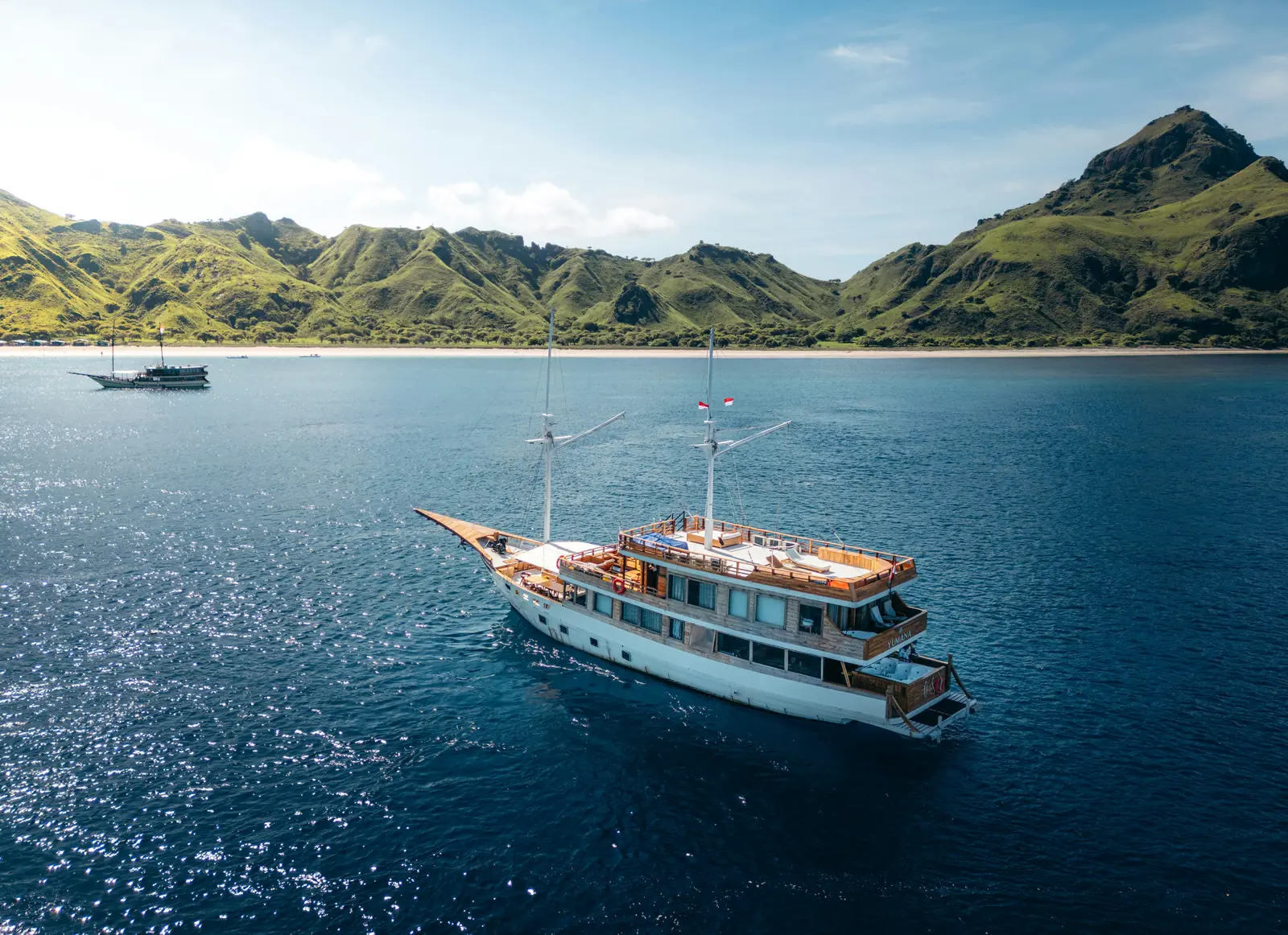 Traditional wooden phinisi liveaboard boat cruising a calm bay among green Komodo islands