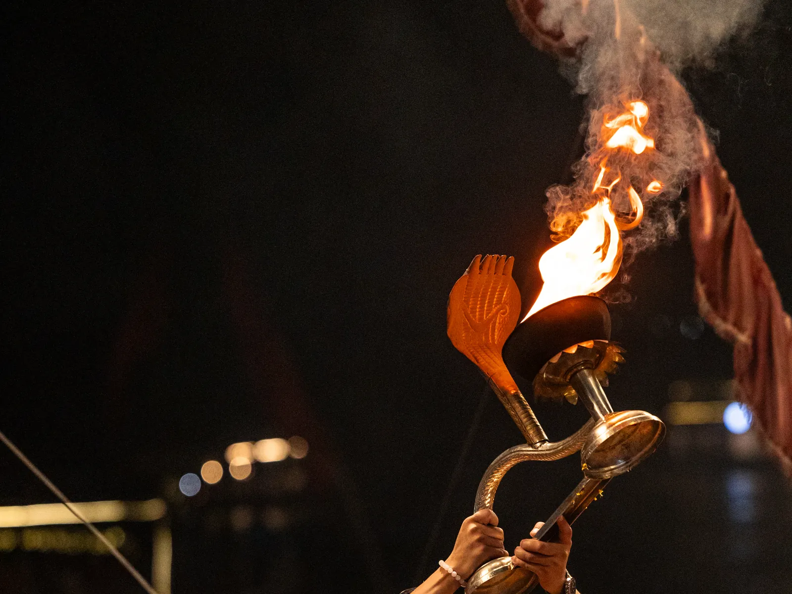 Priest raising a lit brass aarti lamp during an evening Hindu ceremony by the river